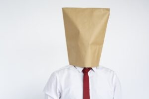 “anonymous man with a paper bag over his head symbolising the work hero identity becoming invisible at work”