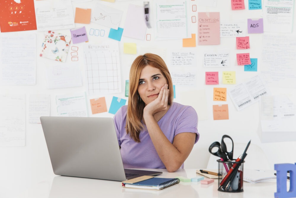 A young woman thinking in front of her laptop with colorful sticky notes, representing the LinkedIn personality in MENA.