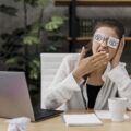 Woman hiding fatigue with sticky notes while yawning after a meeting showing extended meeting recovery time