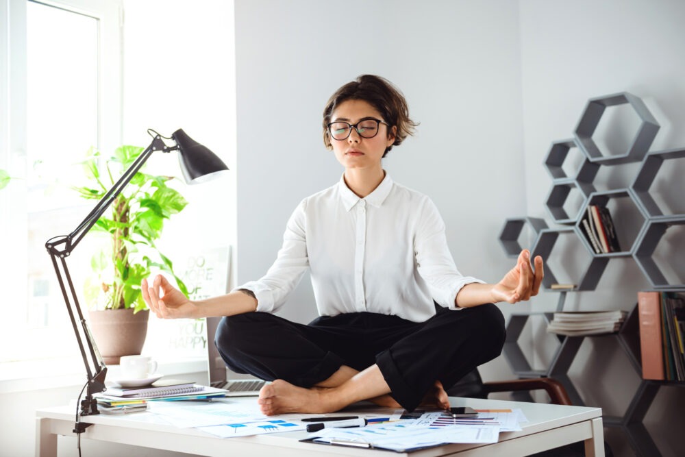 Young businesswoman meditating at her office desk representing work life balance in the Middle East