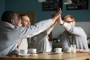 A diverse group of colleagues smiling and giving a high-five at a café, showing the positive energy that comes from genuine connection at work.
