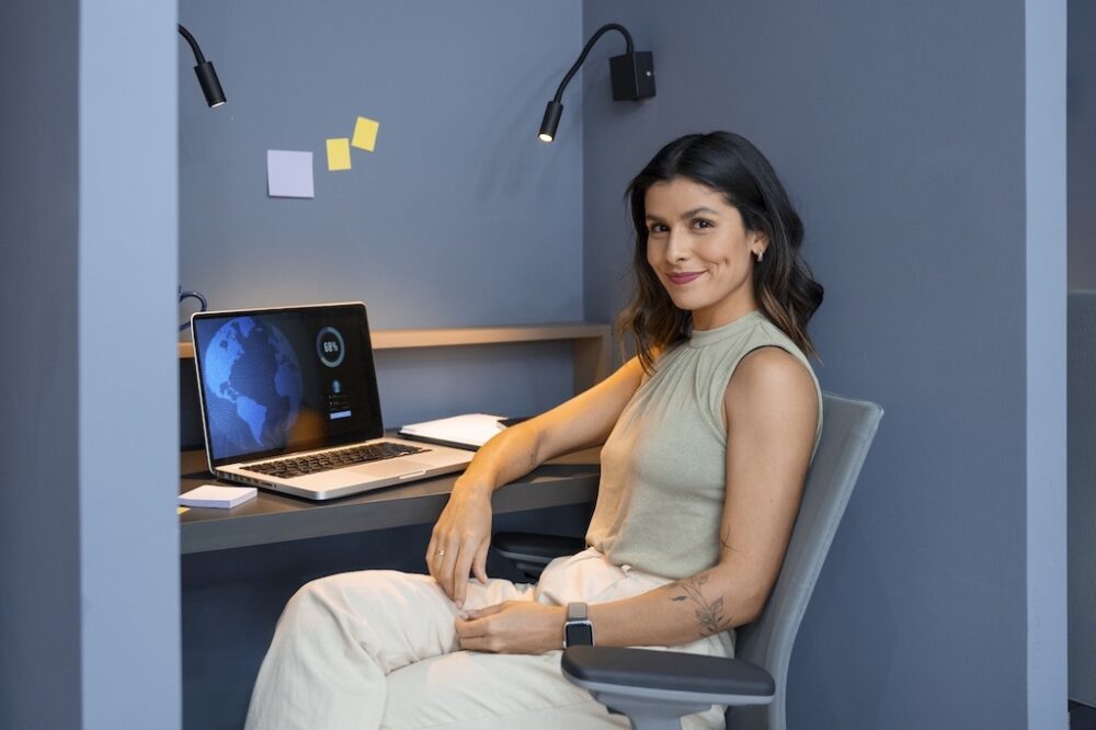 A young woman smiling while using her laptop, representing a confident modern professional embracing a flexible and multi identity career path.